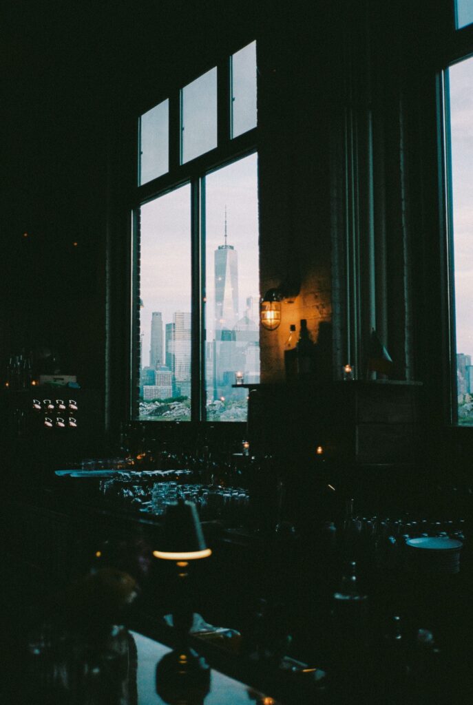 View of the New York City skyline through the large windows of the dark bar area at Battello